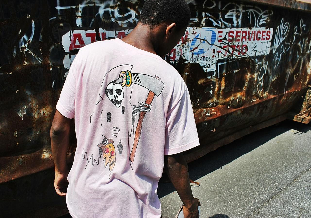 A skateboarder wearing a custom pink t-shirt with an illustrated back print.